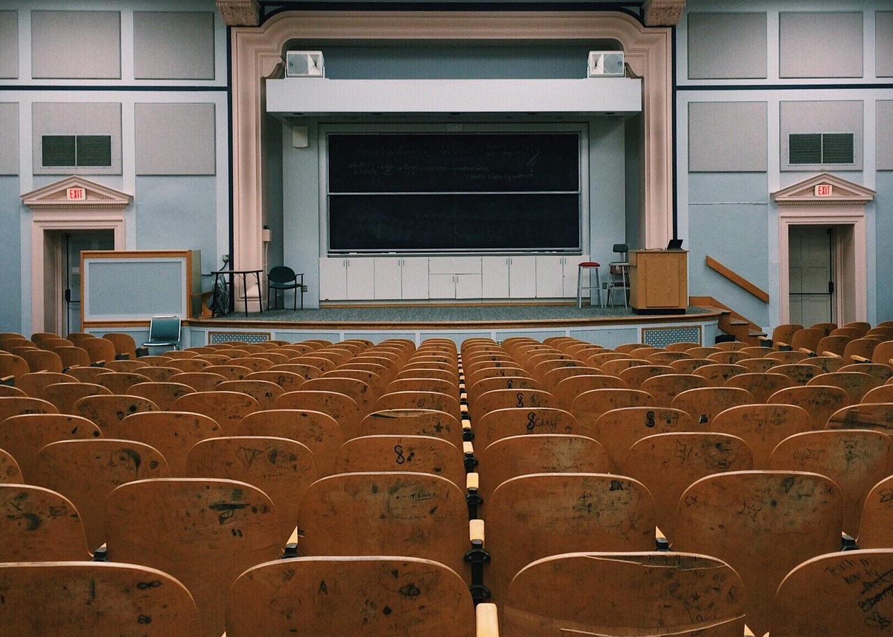 An empty lecture theatre with rows of wooden seats facing a blackboard