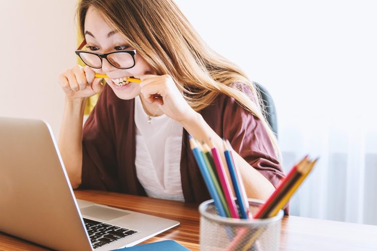 A student at a laptop with a pencil between her teeth