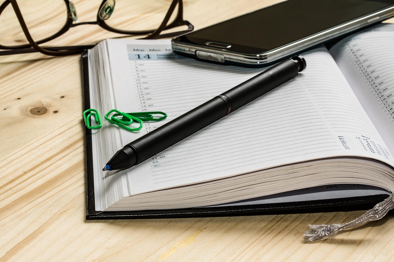A diary, a pen and a phone on a wooden desk