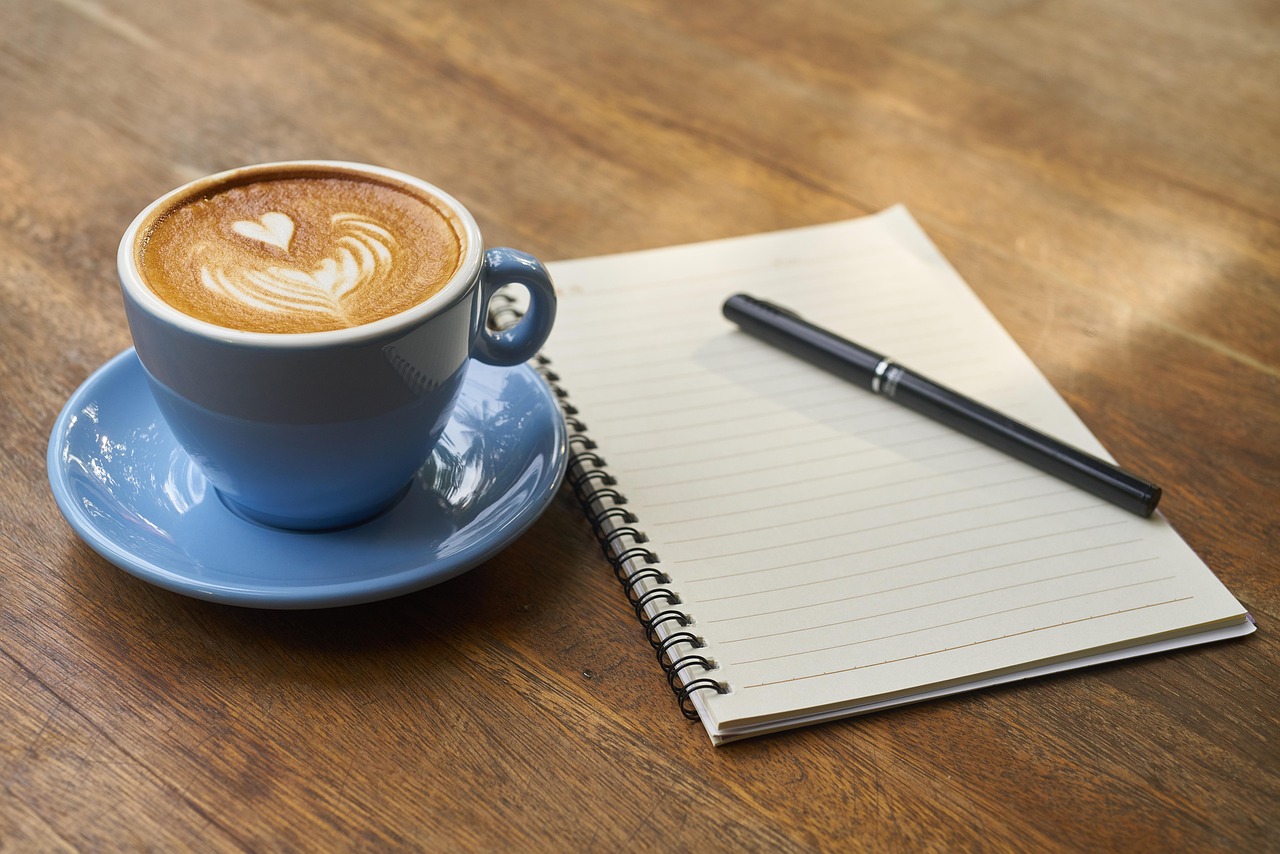 A cup of coffee, a pen and an open notebook