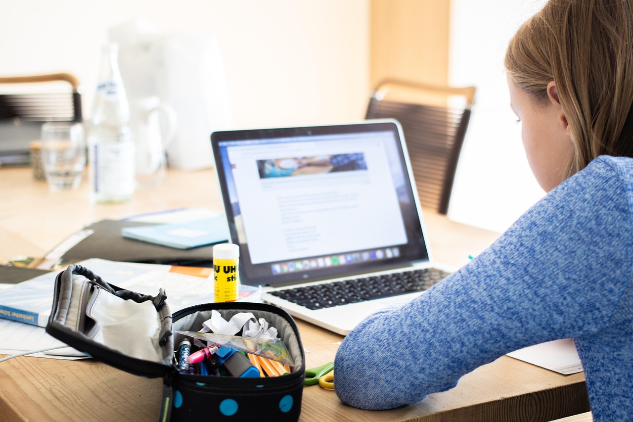 A student working at a laptop with school supplies beside her