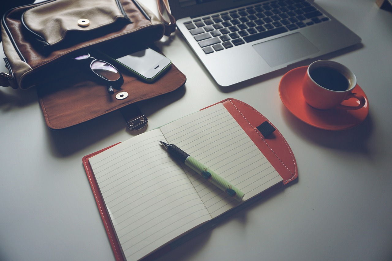 A laptop, notebook, glasses and coffee on a desk