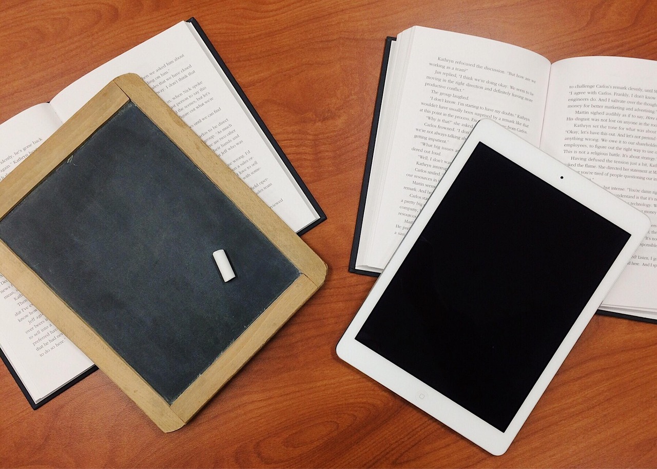 A tablet, a slate and open books on a wooden table