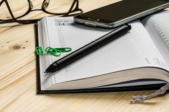 A diary, a pen and a phone on a wooden desk
