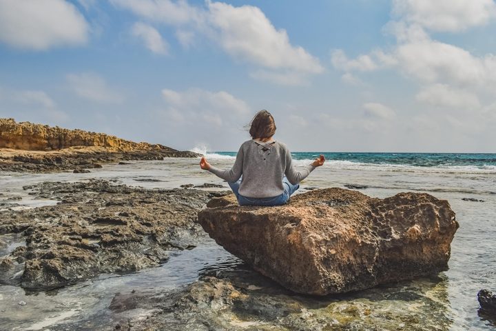 A person meditating on a rock beside the sea