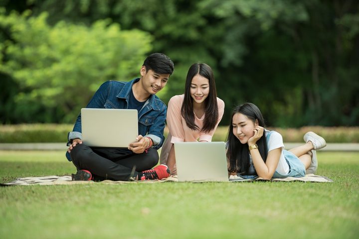 Three students working together on laptops on a lawn